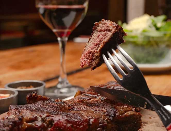 Corte de carne a las brasas con tenedor y copa de vino